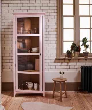 How to style a display cabinet - narrow glass fronted dresser in a pale shade of pink in front of tiled wall with wooden floors