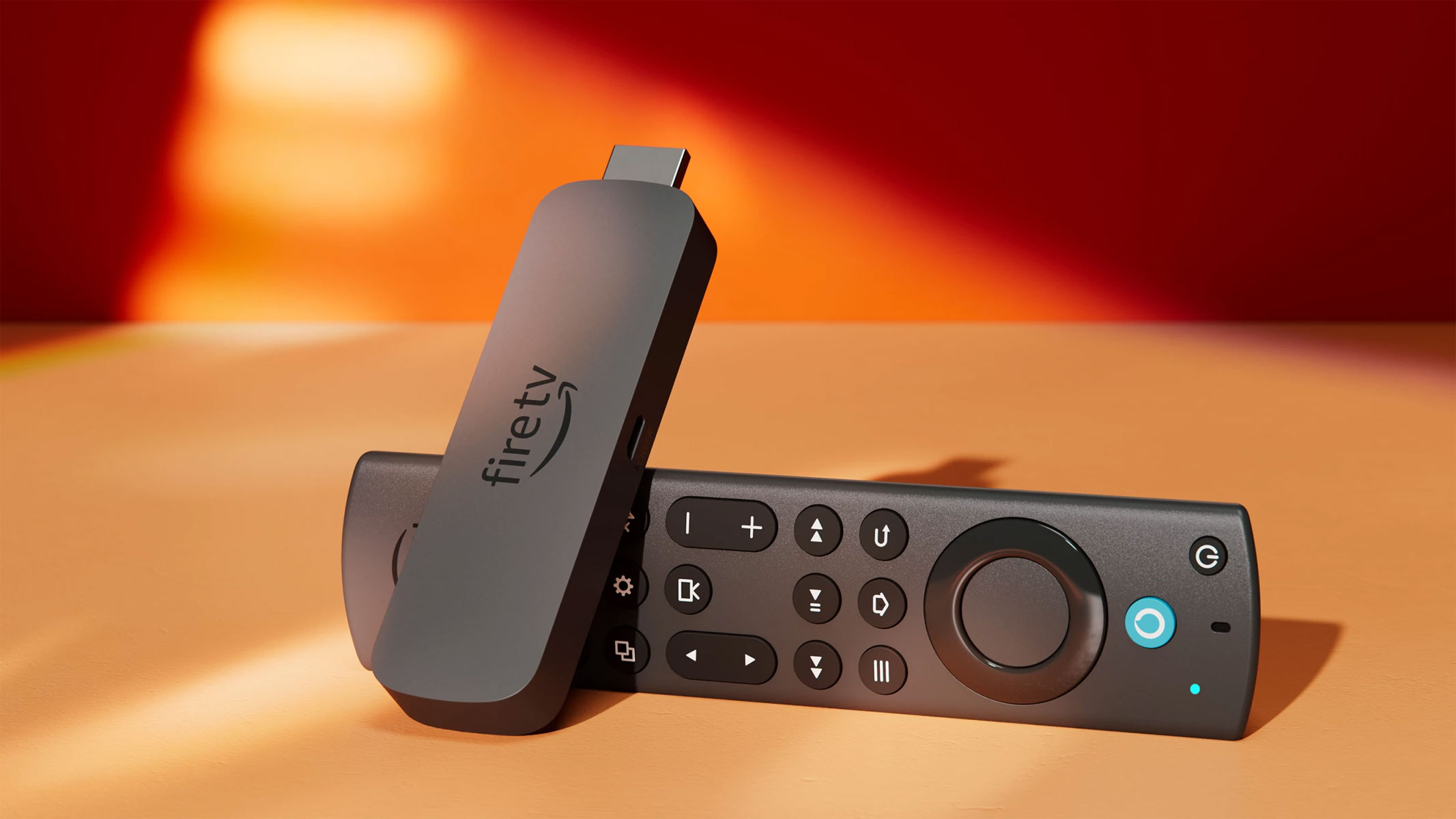 A stick-like device with a HDMI port sticking out the top of it is leaning on a black remote controller, all on an orange surface and background.