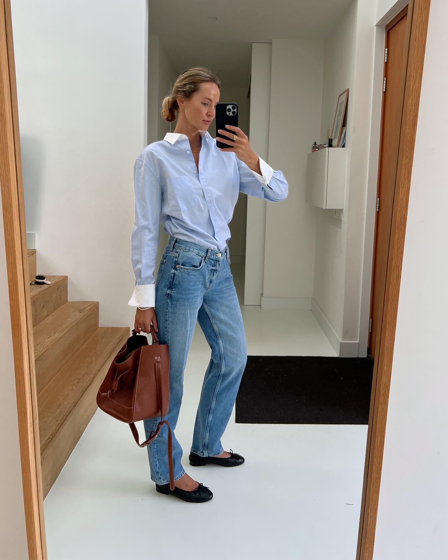 fashion influencer Anouk Yve poses for a mirror selfie wearing a blue button-down shirt with contrast collar and cuffs, jeans, and ballet flats