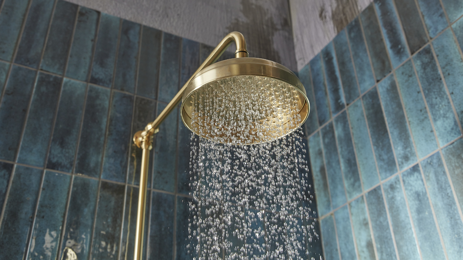 Gold shower head running water with blue rectangle tiles behind