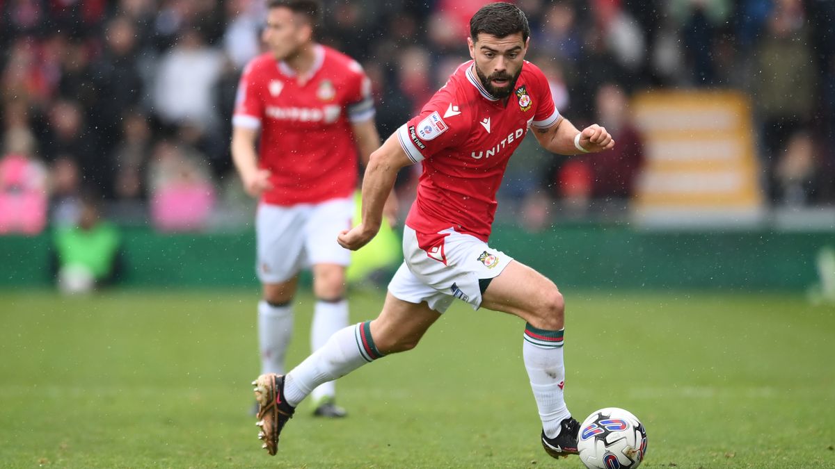 Elliott Lee on the ball for Wrexham in the red shirt and white shorts home strip.