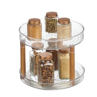 A lazy susan with two clear circiular tiers propped up by three wooden poles, with three spice jars on top and four spice jars on the bottom tier
