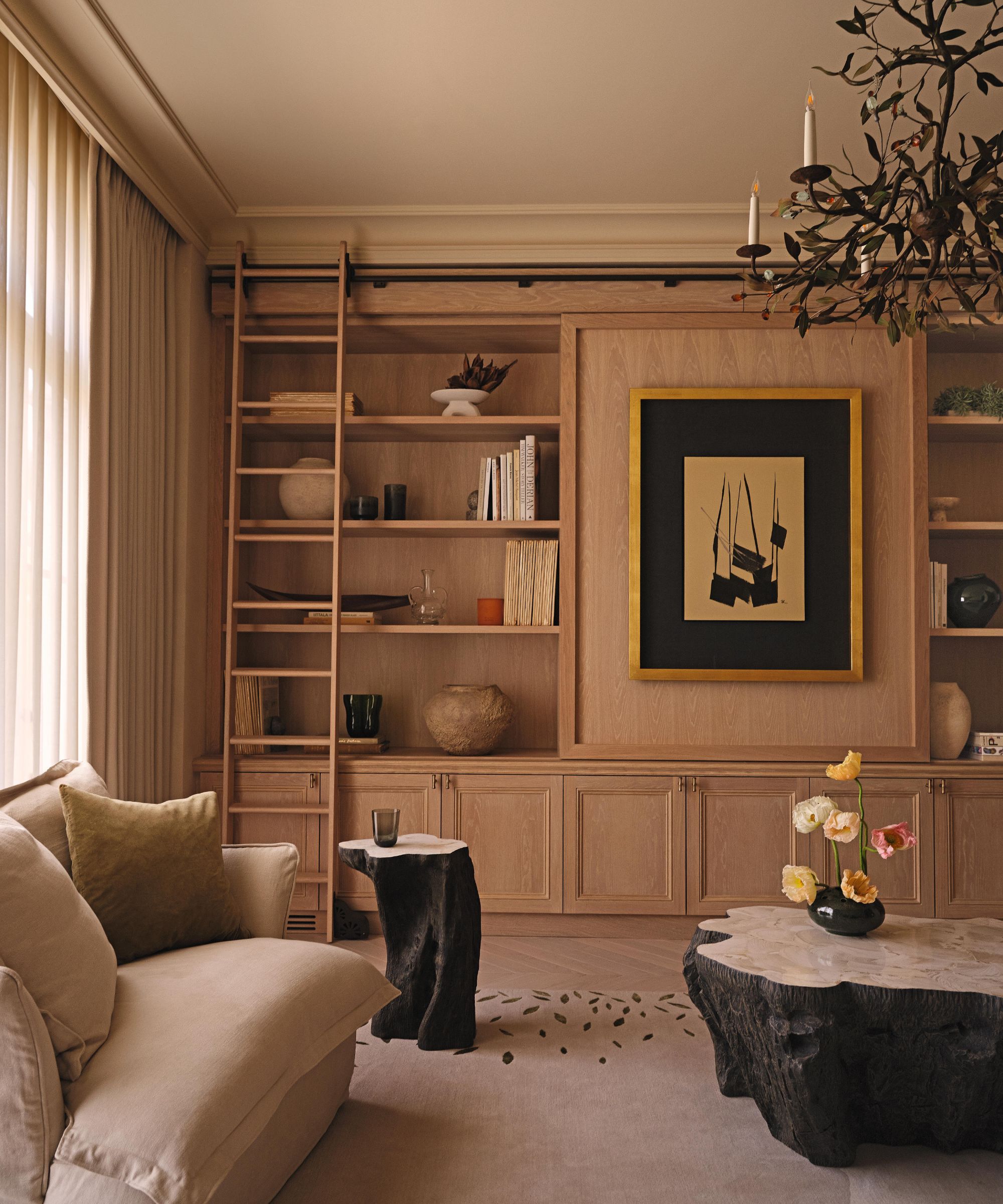 a neutrlal wabi-sabi sitting room with oak bookcases and wooden sculptural tables