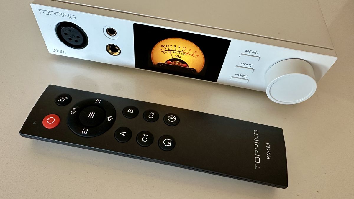The Topping DX5 II on a light-wood table, showing the VU meter, ports and just-seen remote