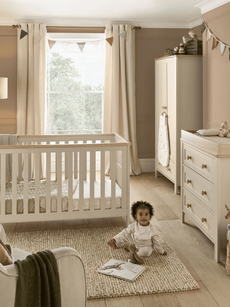 An adorable baby playing in their room surrounded by matching furniture
