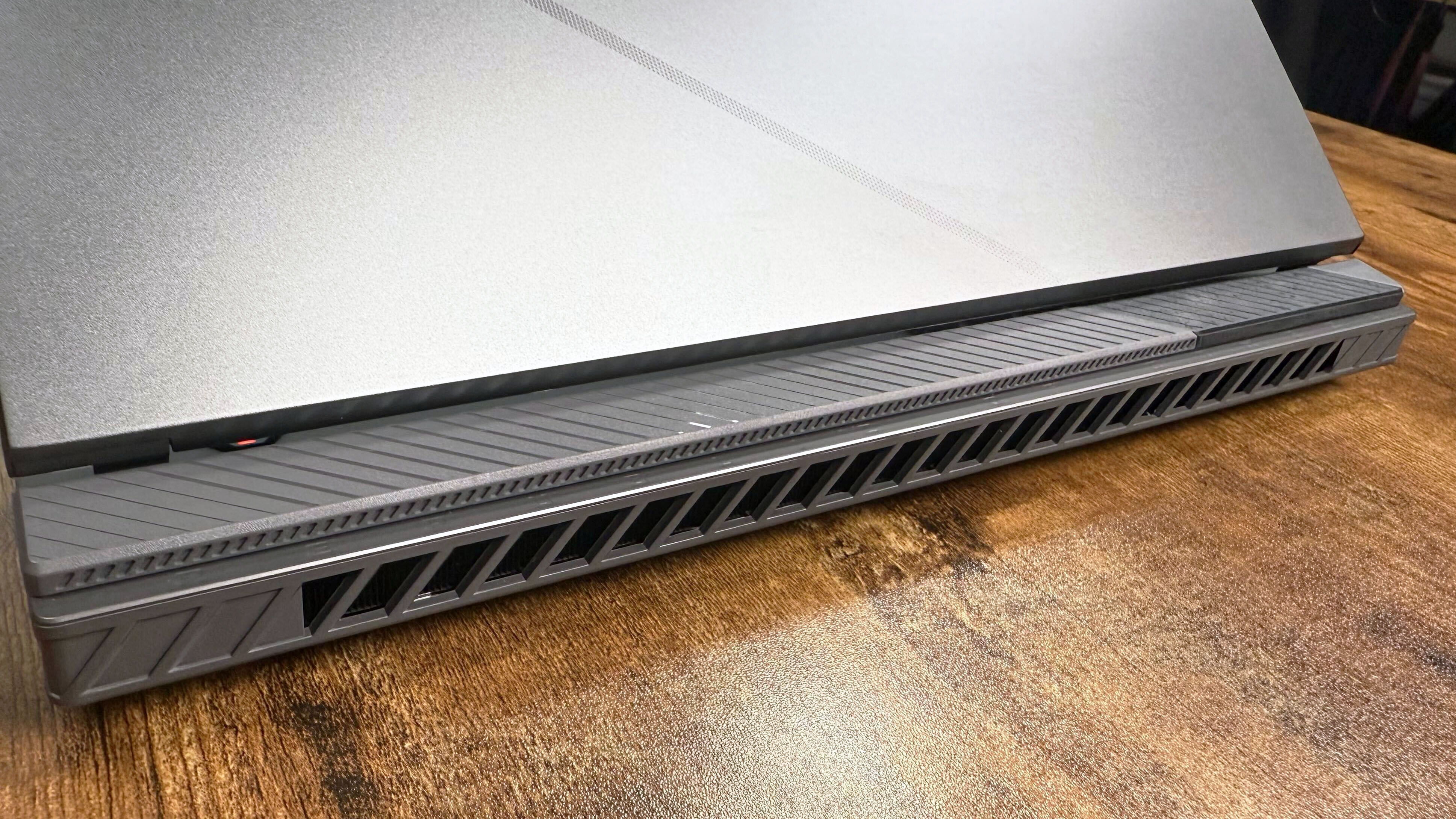 Close up of the rear thermal vents on the Asus ROG Strix G16 (G614FR) gaming laptop on a wooden desk.
