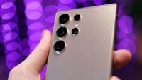 Close up of cameras on a Samsung Galaxy S24 Ultra phone held in a hand with purple lights blurred in the background