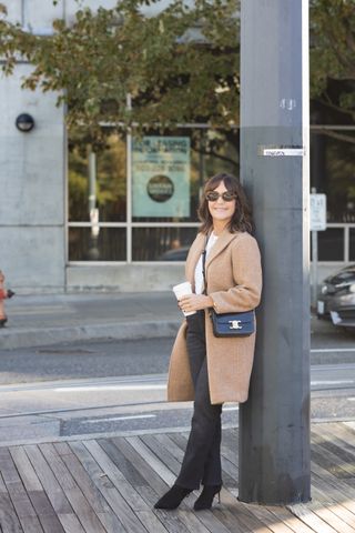 A former Nordstrom buyer wearing a camel coat over a white tee and black jeans.