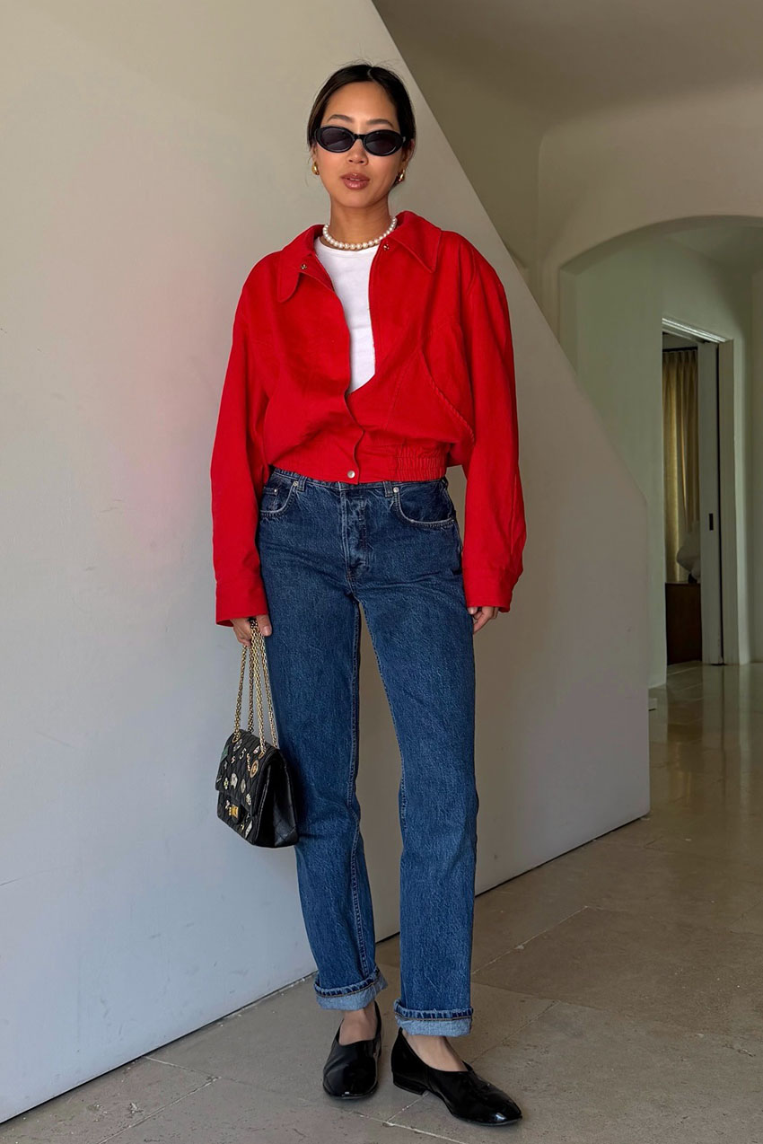 a woman wearing a red button-down shirt, blue jeans, black flats, and black sunglasses