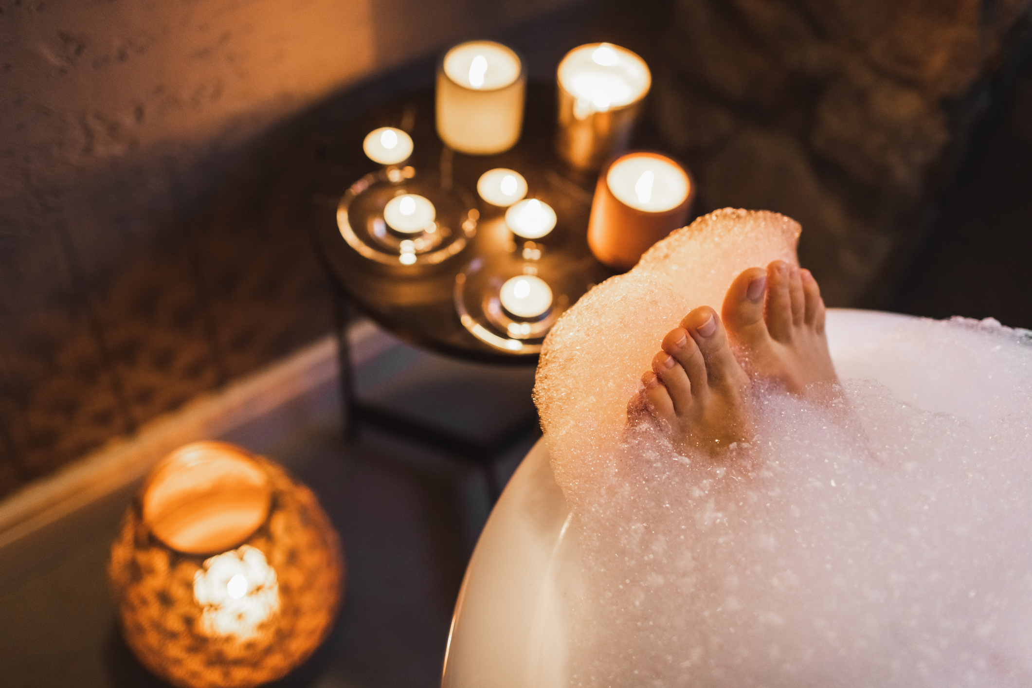 Eine Frau legt ihre Zehen auf den Rand der Badewanne, während sie von Kerzen umgeben ist