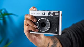 A hand holding a black and gray Fujifilm Instax mini Evo hybrid instant camera