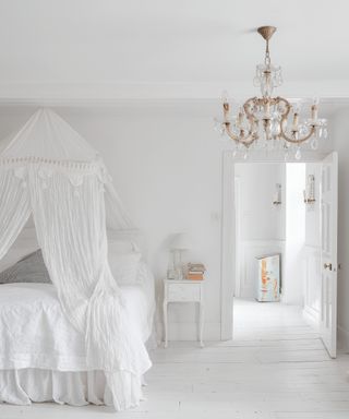 an all white bedroom with white lace curtain and a chandelier