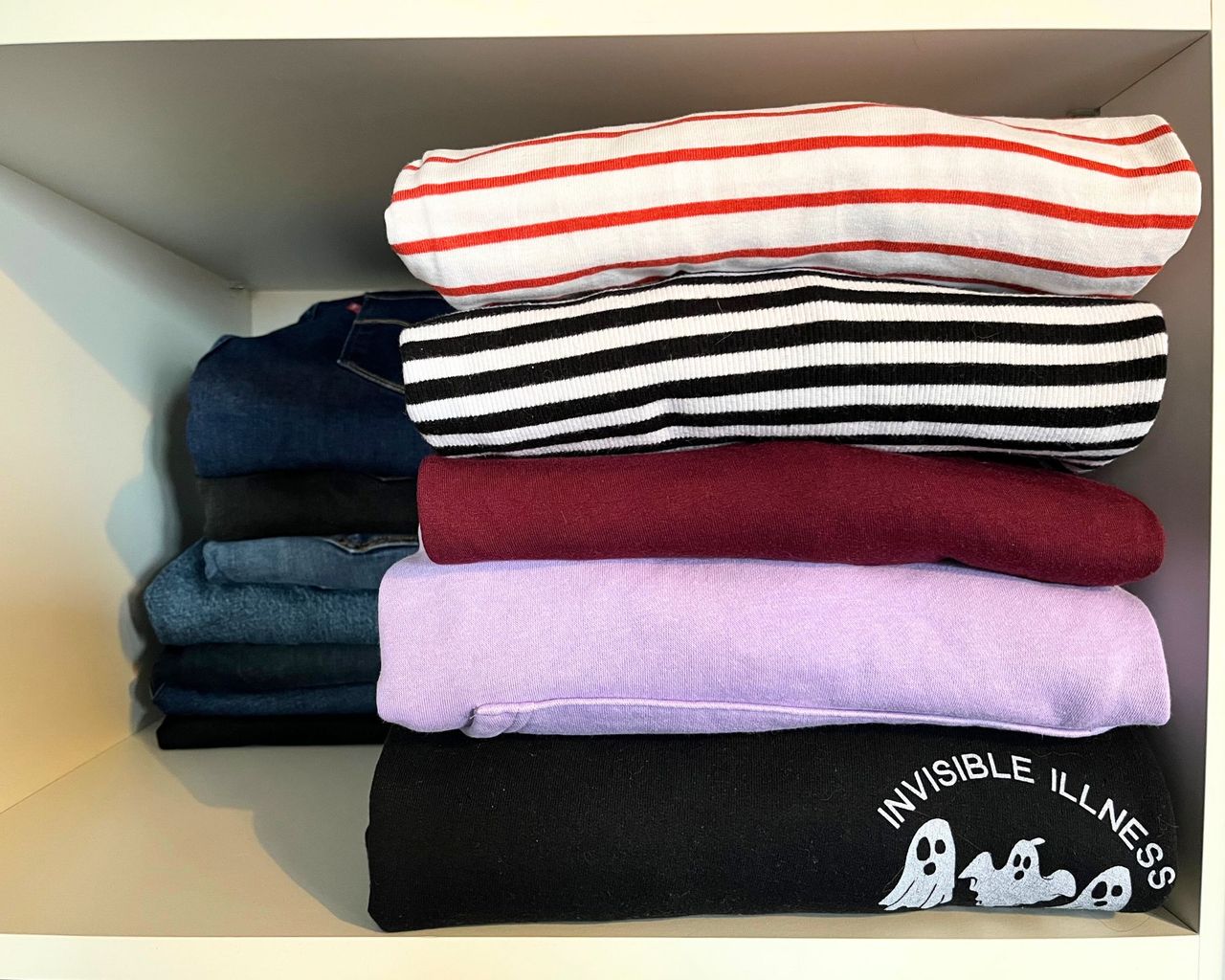 A stack of five neatly folded tops in various colors but all stacked neatly and evenly