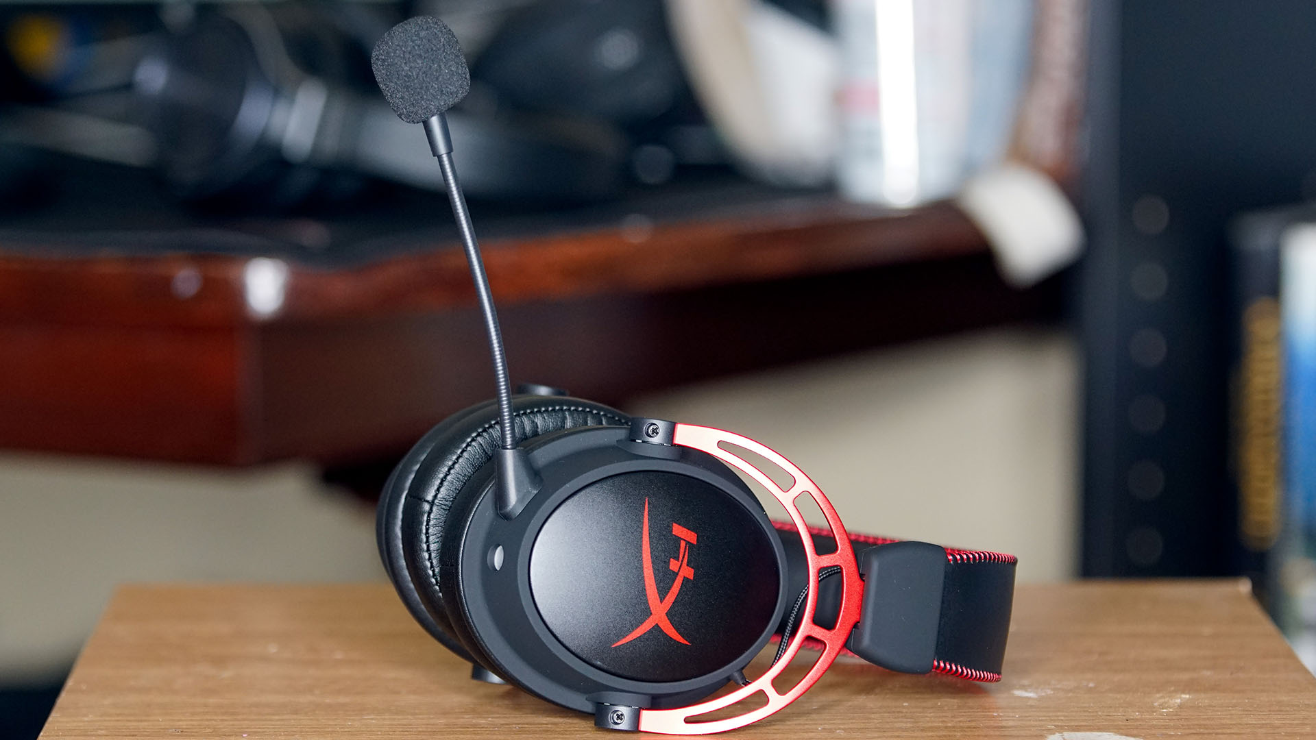Et gaming-headset av typen HyperX Cloud Alpha i svart og rødt ligger på et bord.