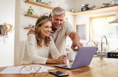 Couple looking at a laptop sitting on the kitchen counter.