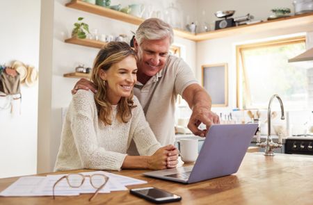 Couple looking at a laptop sitting on the kitchen counter. 