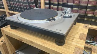 Technics SL-1300G turntable on wooden hi-fi rack in front of bookcase