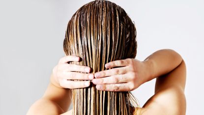 rear view of woman applying conditioner on hair against white background