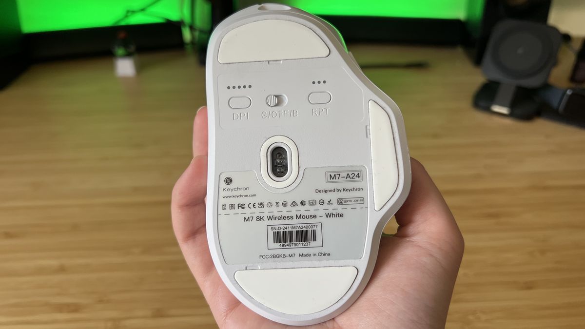 Hand holding Keychron M7 8K gaming mouse and showing underside with sensor and DPI / polling rate indicators