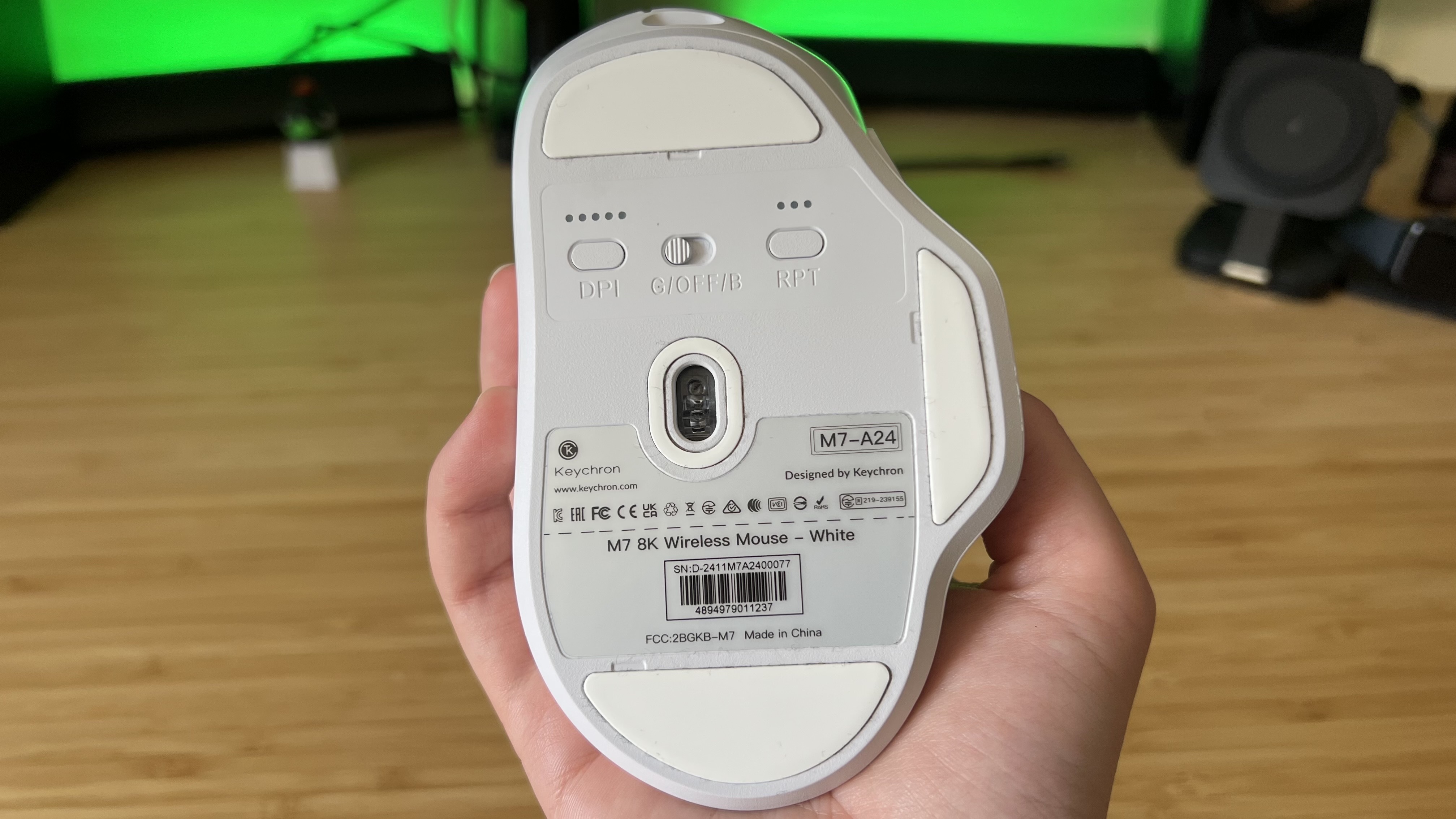 Hand holding Keychron M7 8K gaming mouse and showing underside with sensor and DPI / polling rate indicators