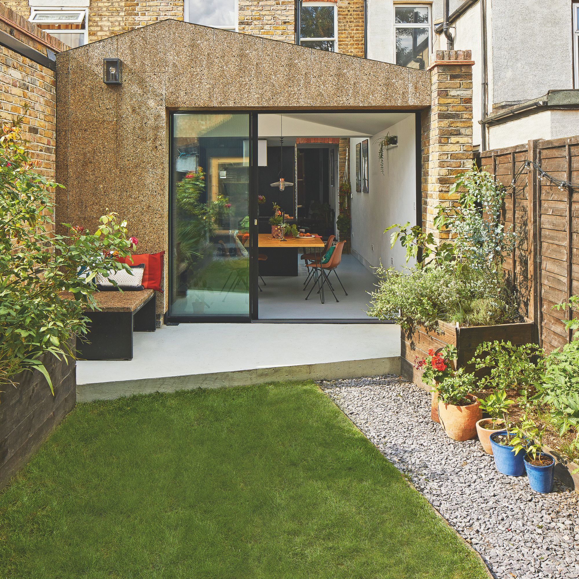 Rear of a house with a small garden laid to lawn, with gravel and some pots on the right hand side