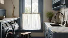 Blue and white laundry room with marble countertops and large window with cafe curtains