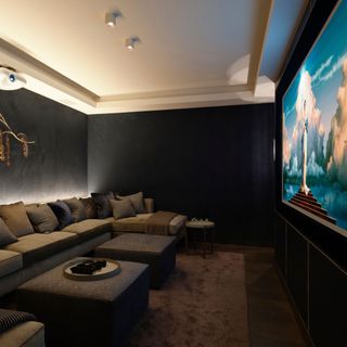 Home cinema with comfy u-shaped sofa, footstools, dark walls and large screen