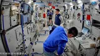 three male astronauts float inside a white-walled space station module