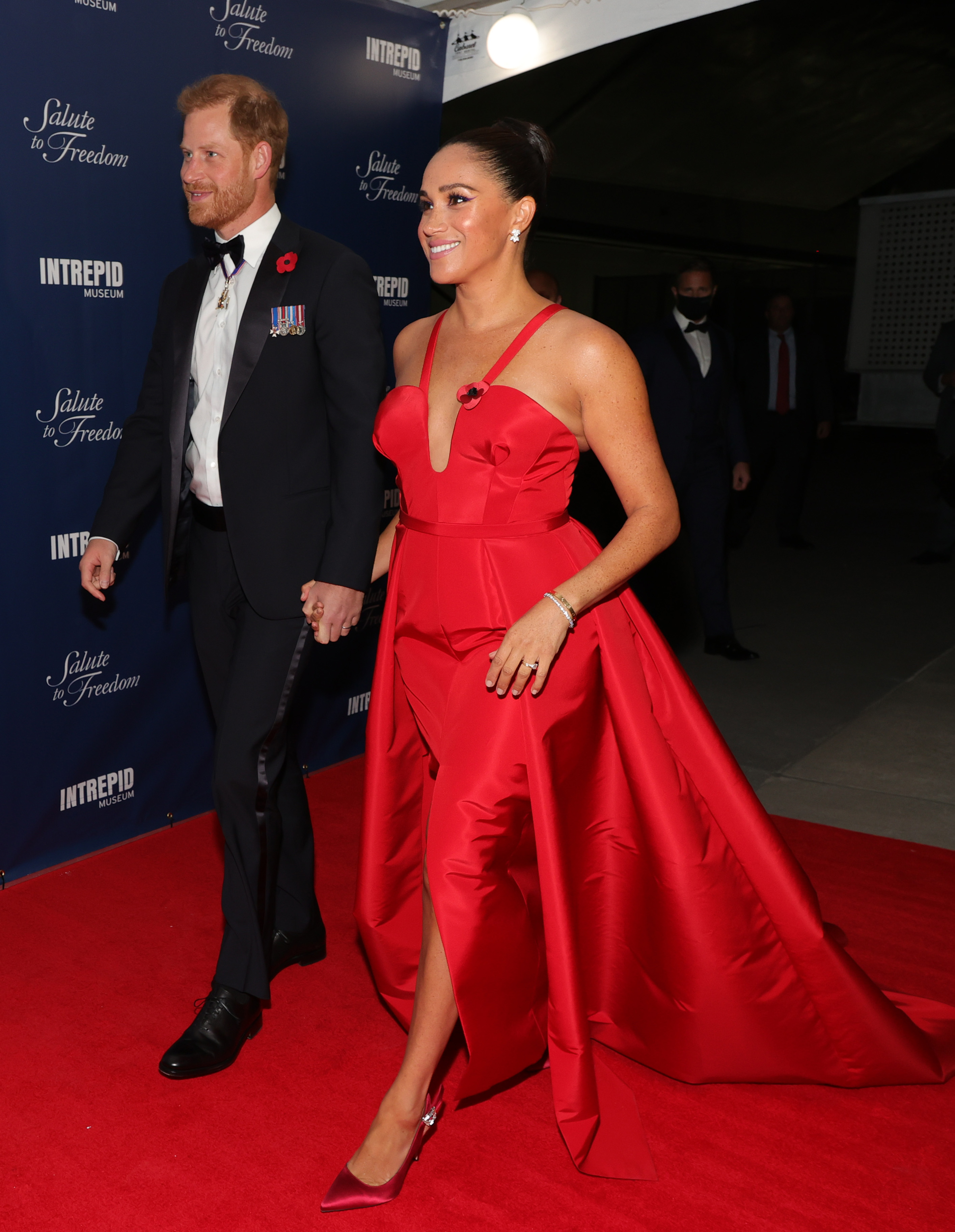 Meghan Markle in a red gown walking with Prince Harry on the red carpet