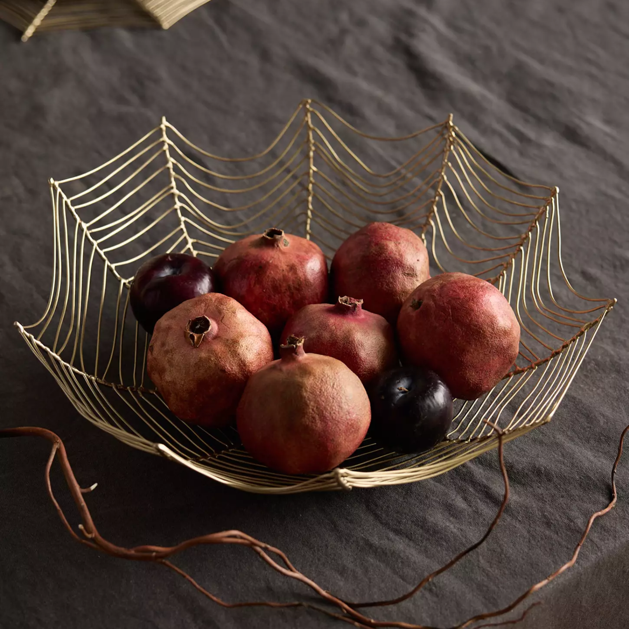 a spider web-like fruit bowl holding an assortment of pomegranates 