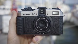 Pentax 17 compact film camera front-on, in the hand with boats in background