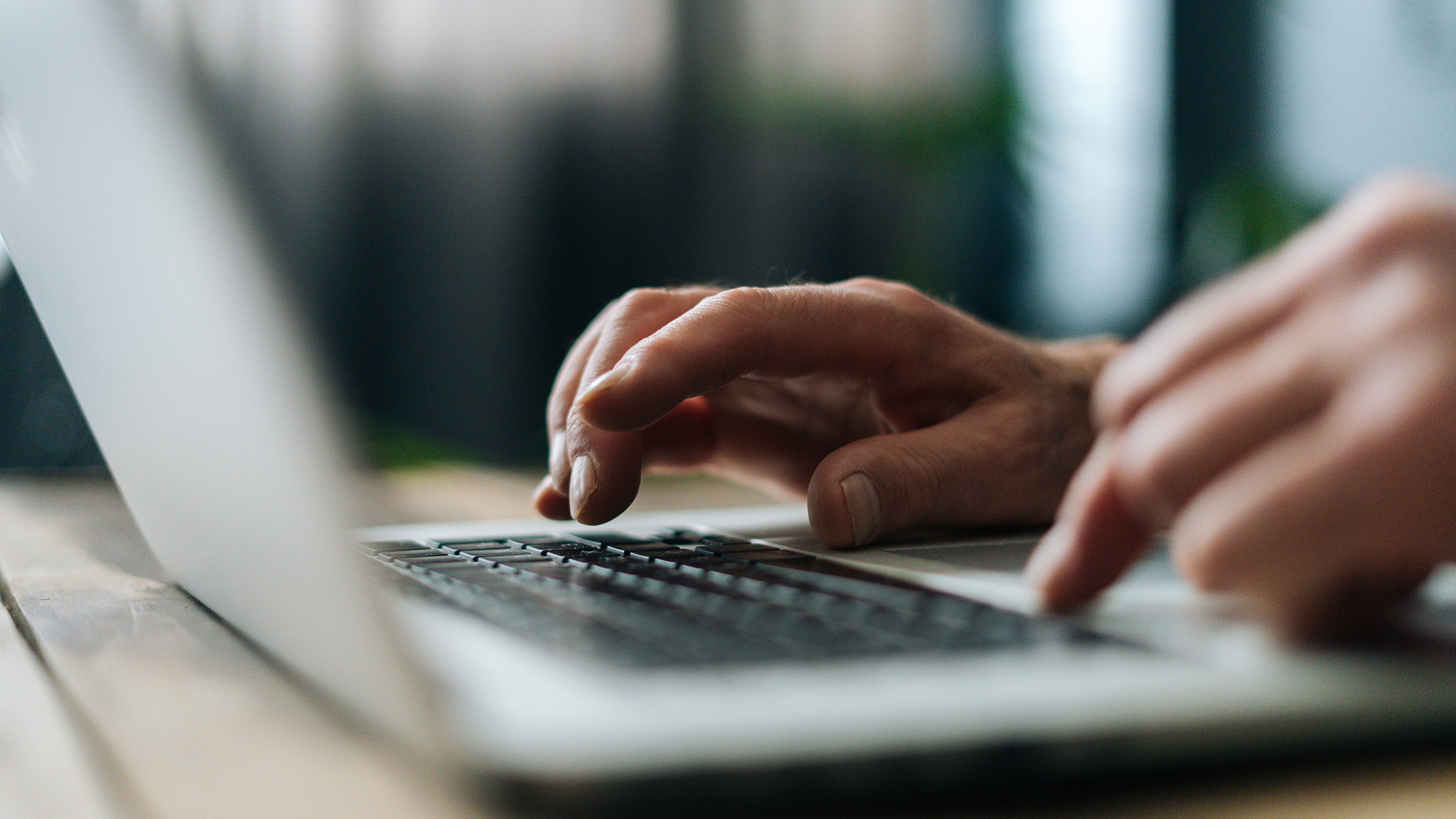 A man types on a laptop, only his hands showing.