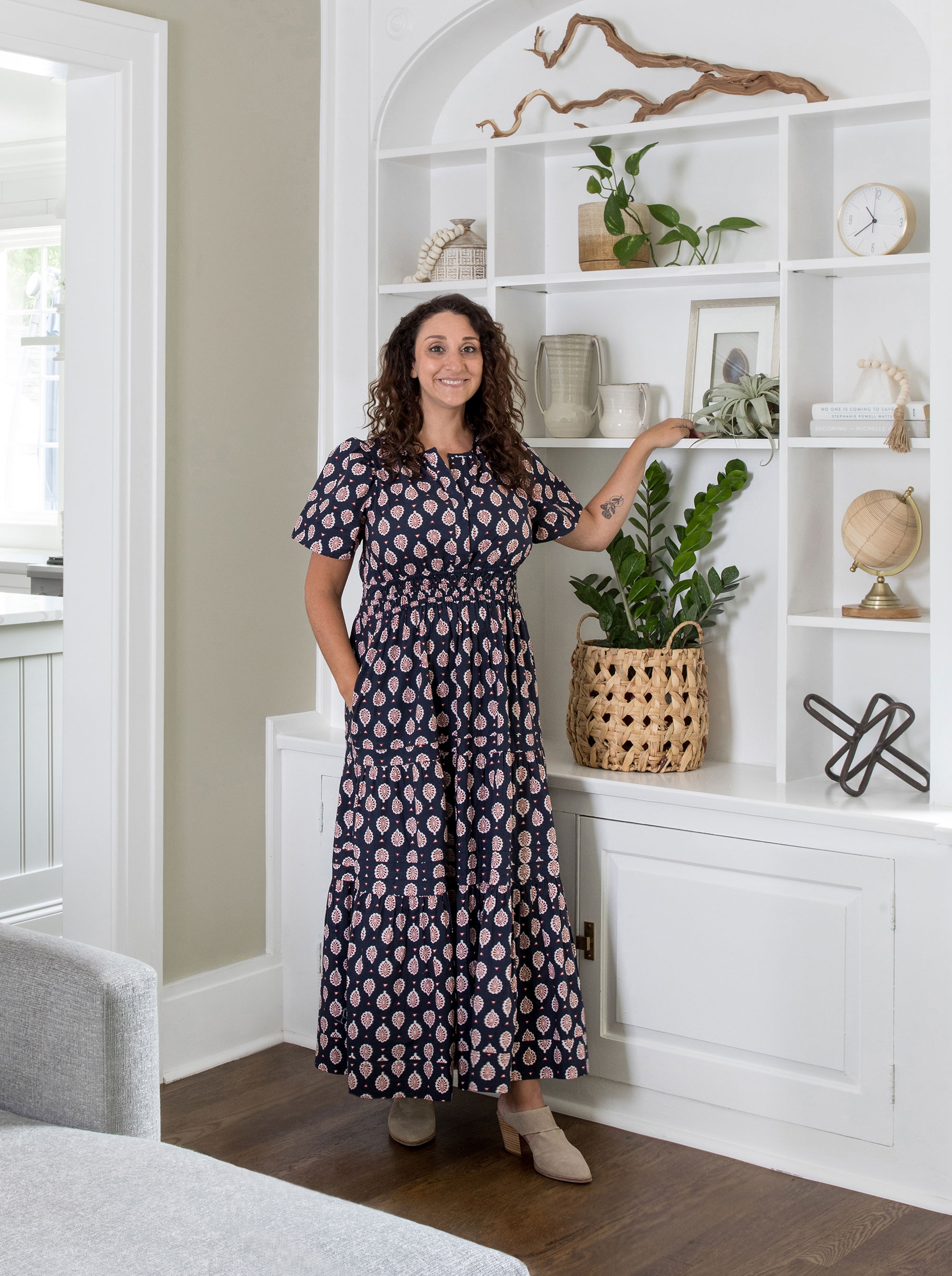 Danielle Chiprut designer in patterned dress standing in living room with alcove shelves