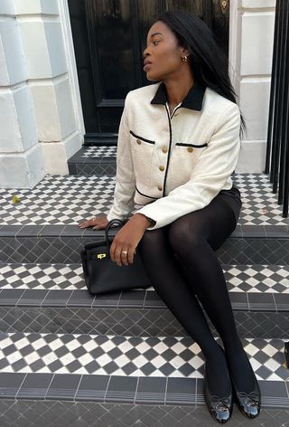 best womens shackets shown on a woman sitting on a stoop wearing a white jacket with a black mini skirt, black tights, and black ballet flats