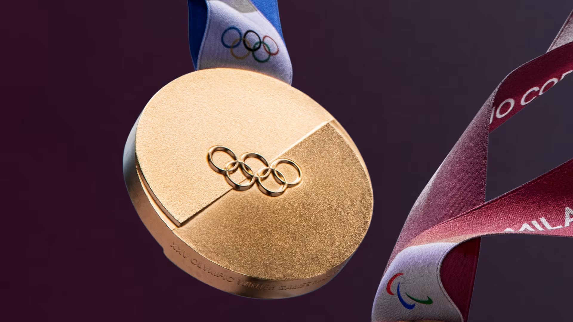A close-up, angled view of the gold medal highlights its textured surface, the prominent "XXV Olympic Winter Games" inscription on the rim, and the accompanying blue and purple ribbons.