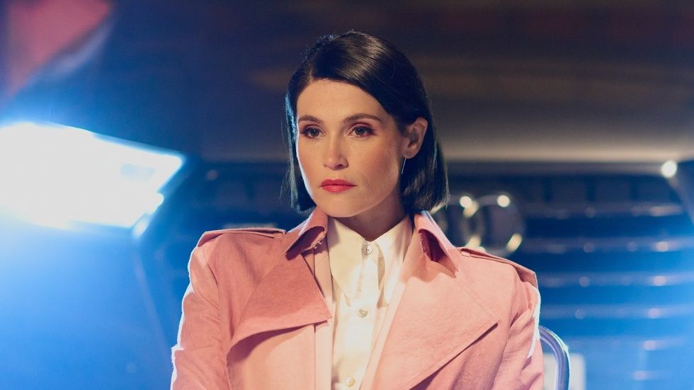 British actor Gemma Arterton, hands folded wearing a dusty pink mac, in new Disney Plus heist drama Culprits. 