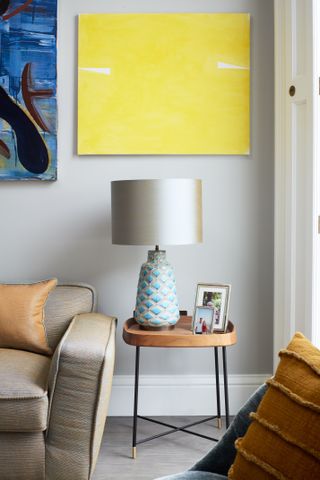 A small table with lamp and photos in front of yellow wall art.