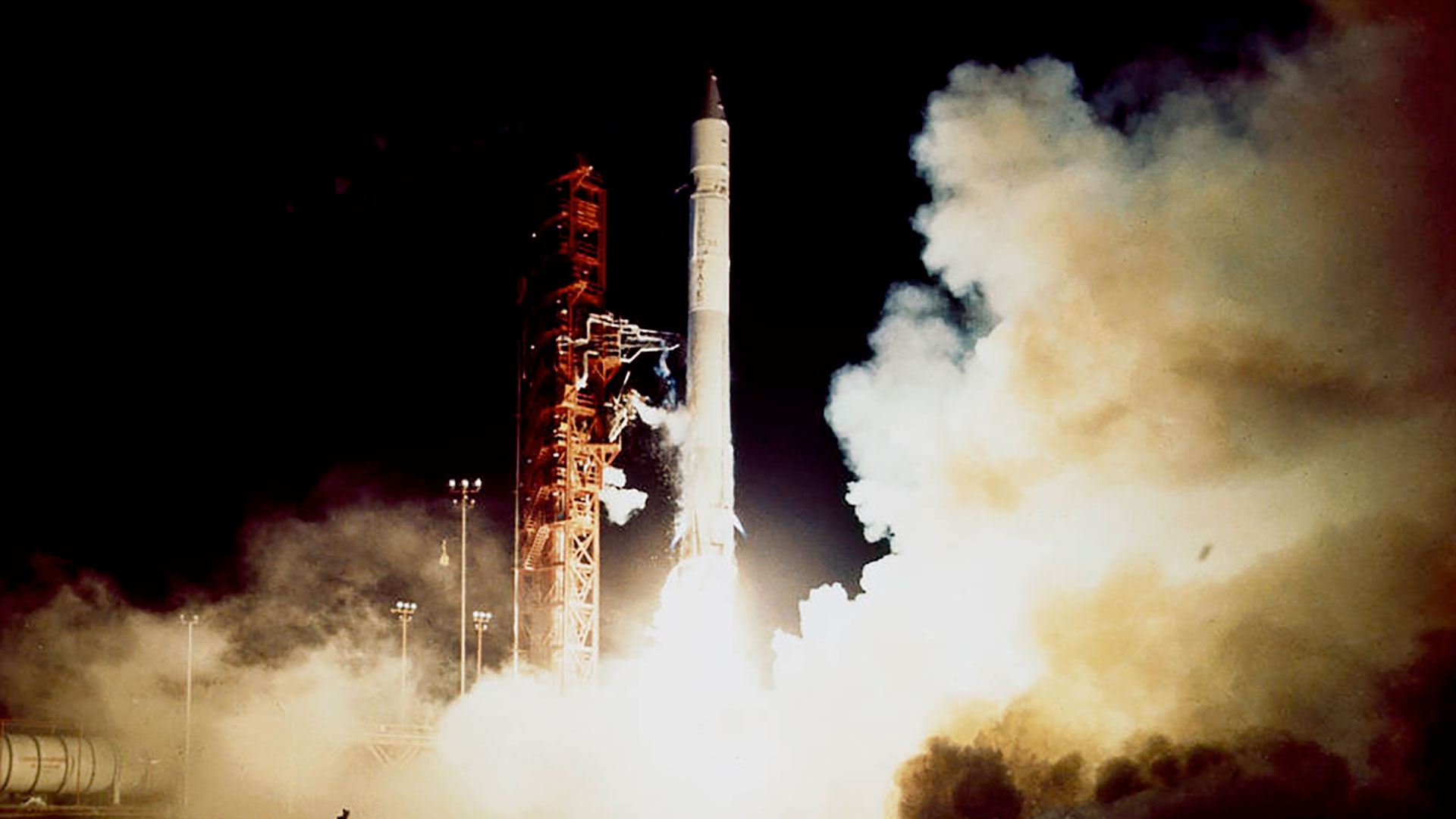 a white rocket rocket lifts off its launch pad, lighting the night sky with its plume.