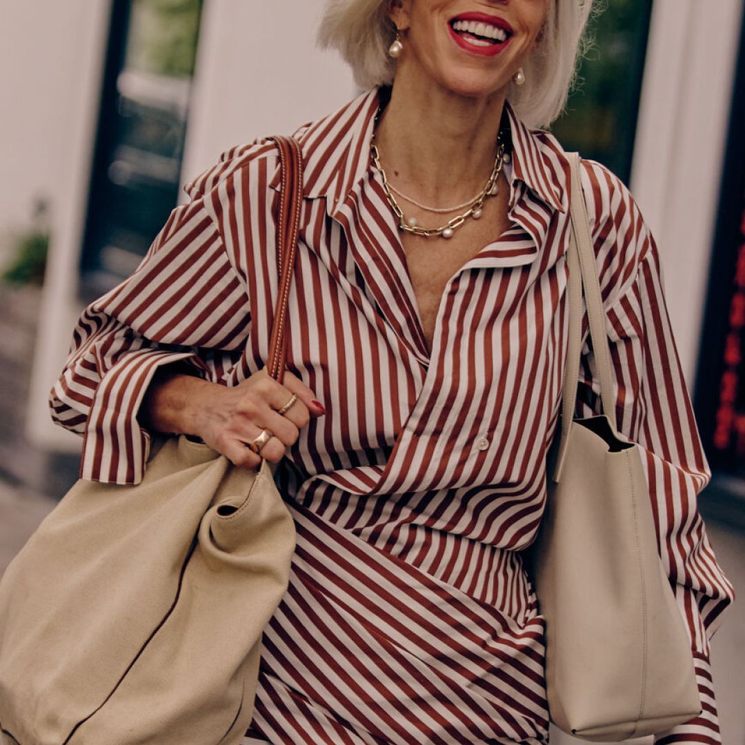 a woman smiling in a striped red dress carrying two white tote bags at new york fashion week
