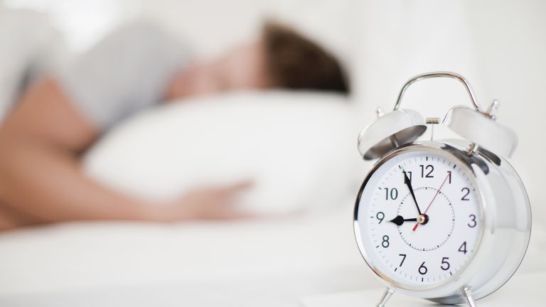 Man sleeps behind an alarm clock resting on a bedside table