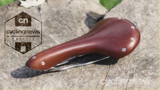 A brown leather saddle stands on a piece of wood
