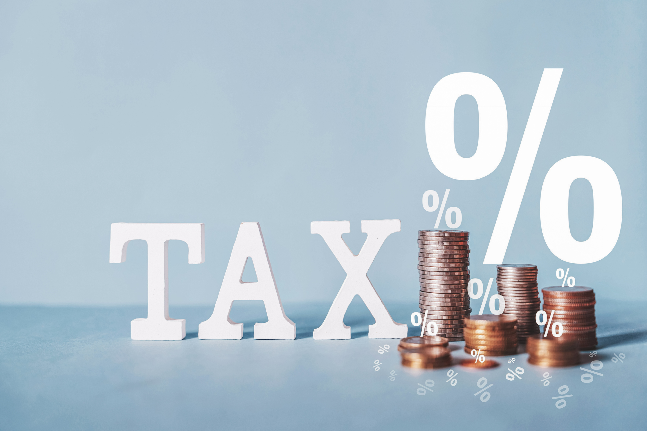 Wooden blocks spelling out "tax" with stacks of coins and percentage signs