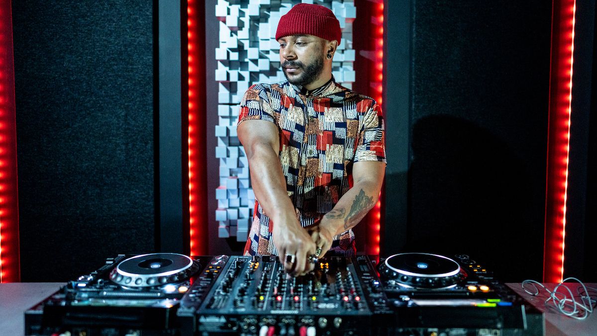 Man wearing a red hat stood behind a set of DJ decks