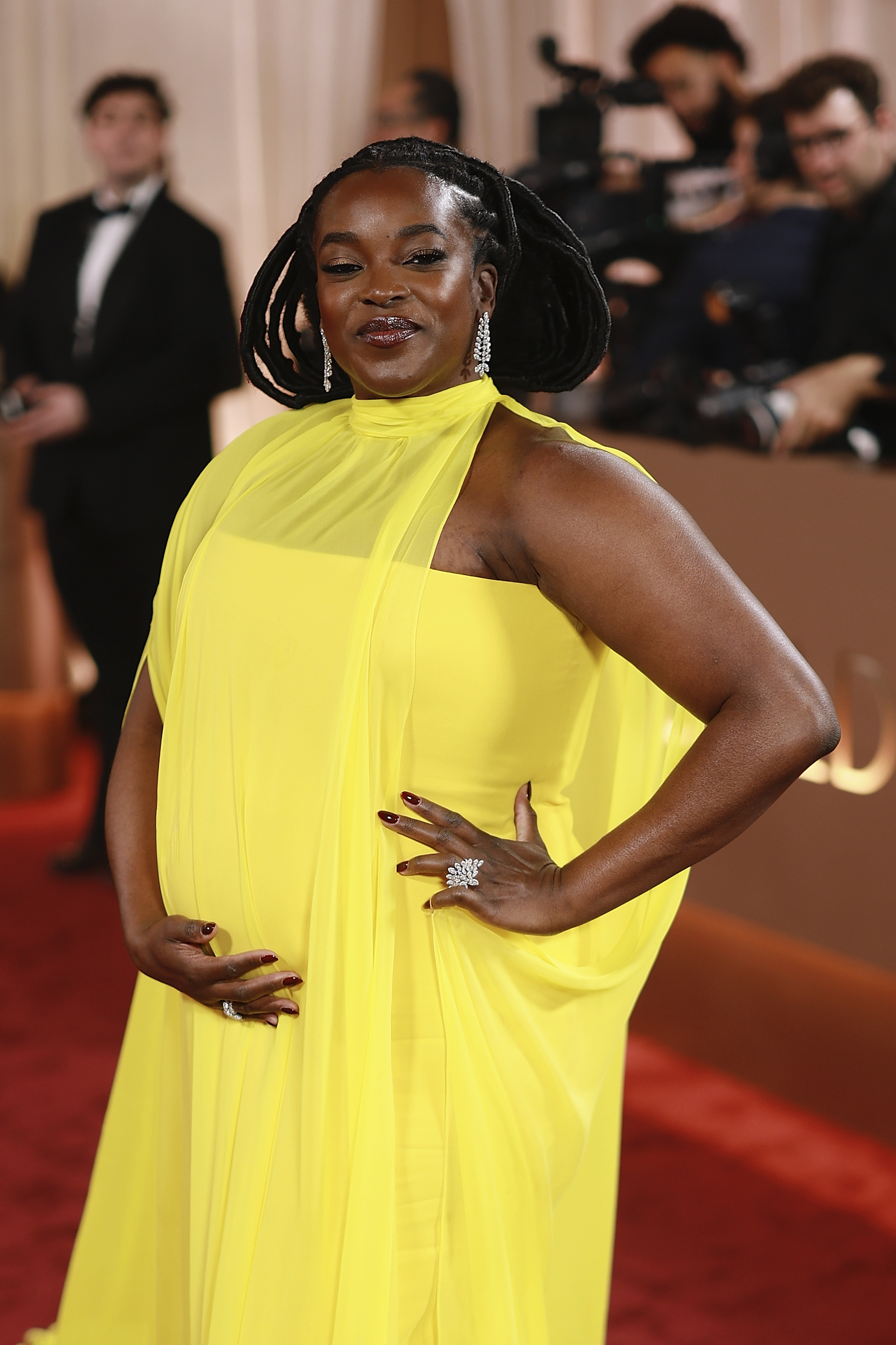 a black woman attends a red carpet awards show wearing a yellow gown