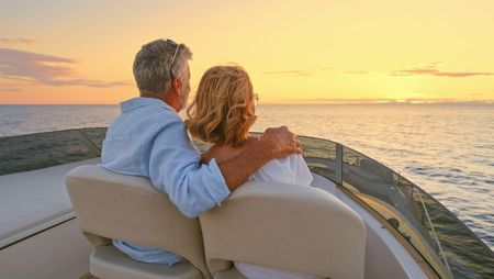 Senior couple driving luxury yacht in sea against sky.
