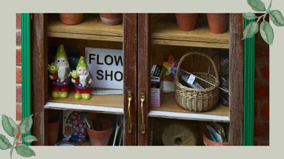 Two garden gnomes on display in a garden storage cabinet with a flower show sign to support the gnome ban being lifted at the RHS Chelsea Flower Show 2026