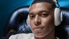 Kylian Mbappe wearing Loewe Leo headphones in a big leather chair with blue light behind him