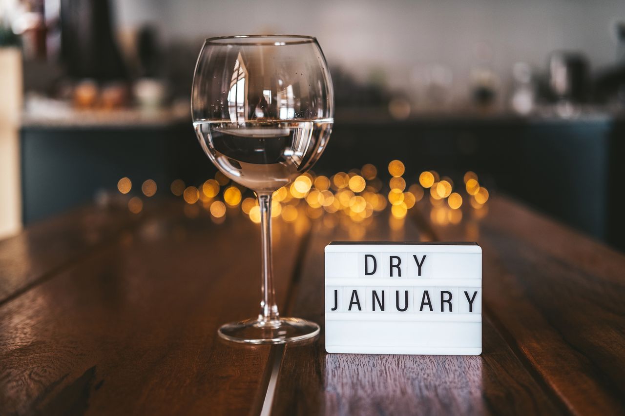 A wine class with a neon sign that reads &#039;DRY JANUARY&#039; on a wooden table, in front of string LED lights in a kitchen.