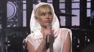 Miley Cyrus wearing a white hood while performing on SNL