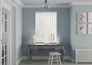 blue painted home office space with white vertical blinds a gray dresser/desk and white simple gallery wall